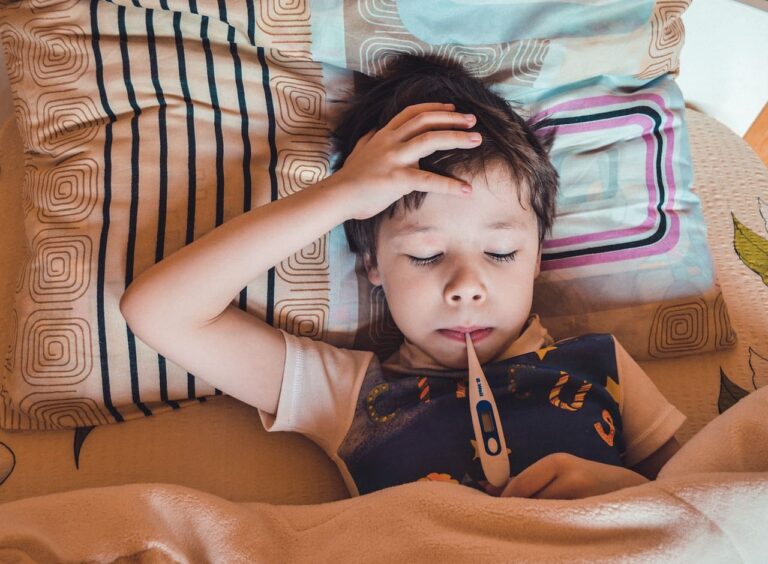 Krankes Kind liegt im Bett mit Fieberthermometer im Mund