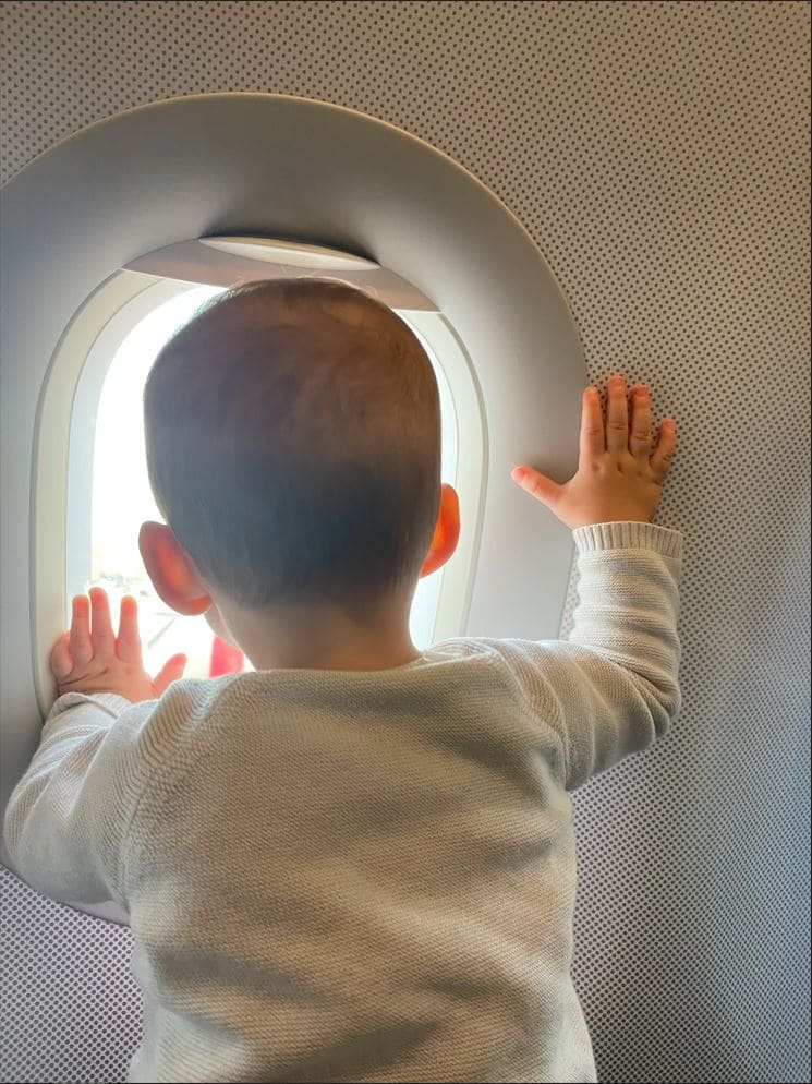 Kind schaut durchs Fenster aus dem Flugzeug.