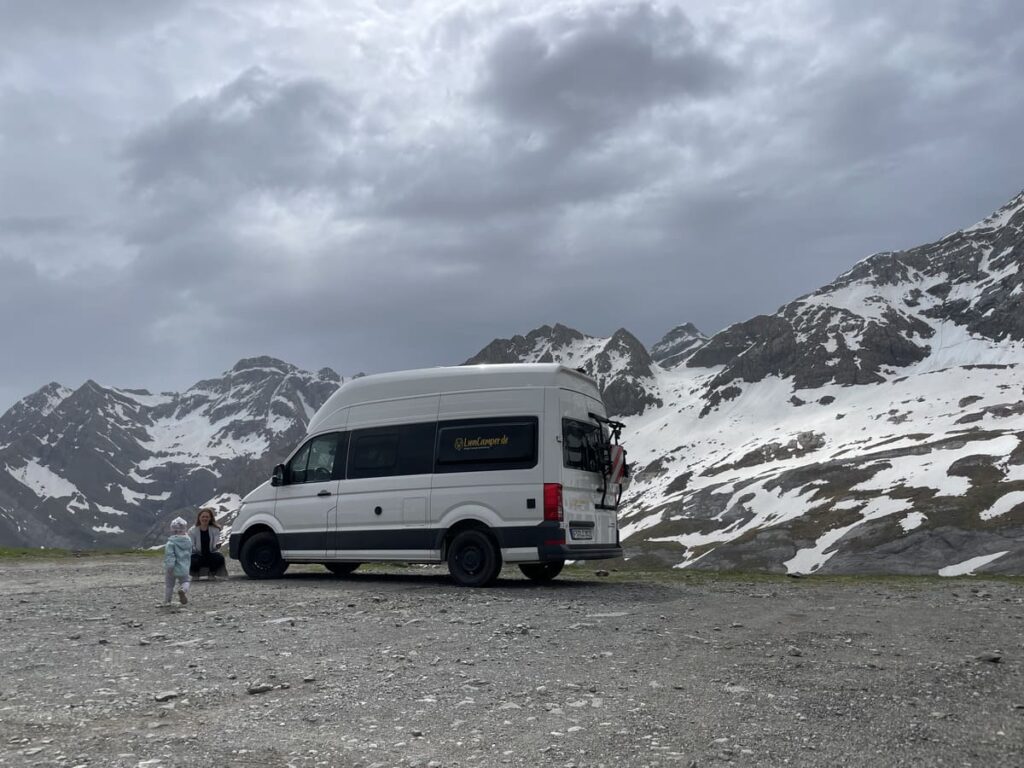 weißes Wohnmobil auf Schotter vor einem Schneeberg