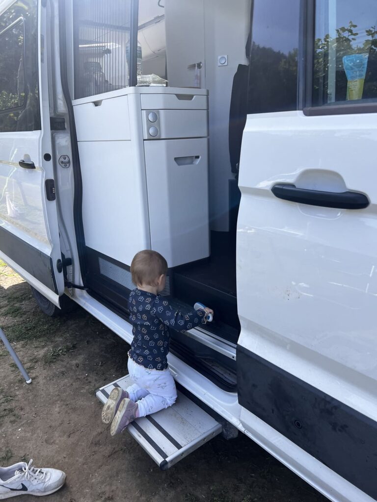 Kind kehrt kniend auf einer Stufe mit dem Handbesen am Wohnmobil