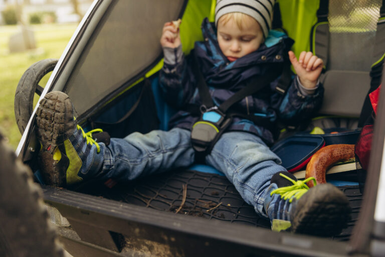 Kind mit ausgestreckten Beinen im Fahrradanhänger, schaut auf die Fußmatte